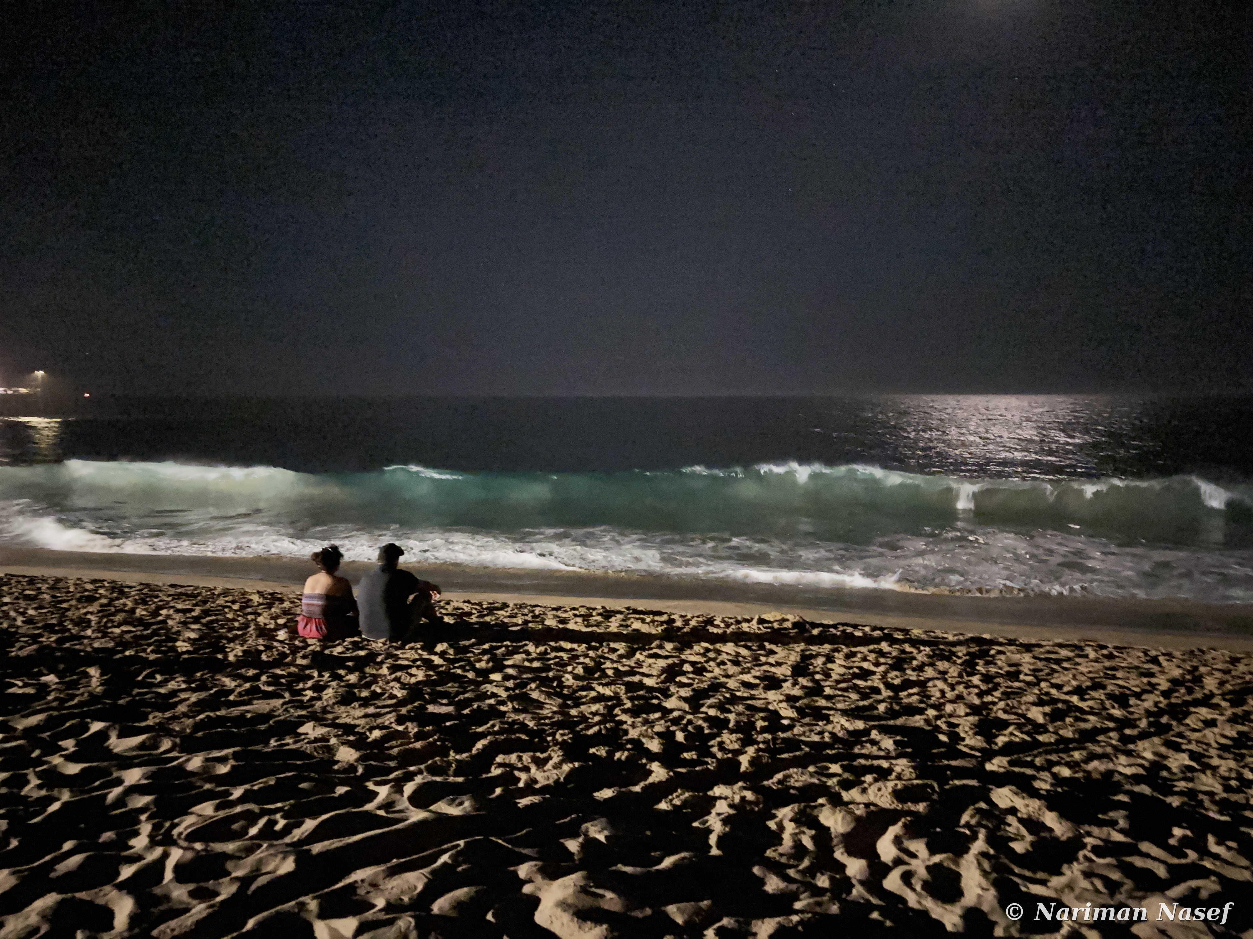 A couple watching waves break under moonlight
